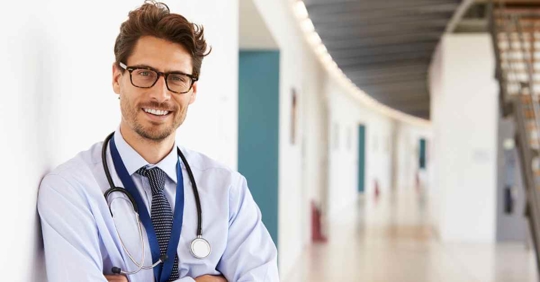 A doctor smiling at the camera as he stands in the hallway of his practice