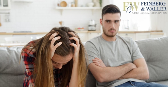 A man and woman sitting on a couch; the woman holding her head in her hands.