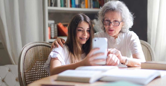 A young girl using a cell phone to take a selfie with her grandmother.