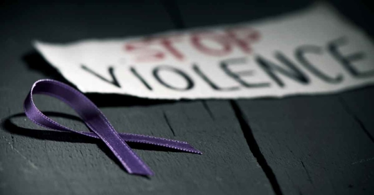 A purple ribbon signifying domestic violence awareness. Behind it is a sign reading "Stop Violence"