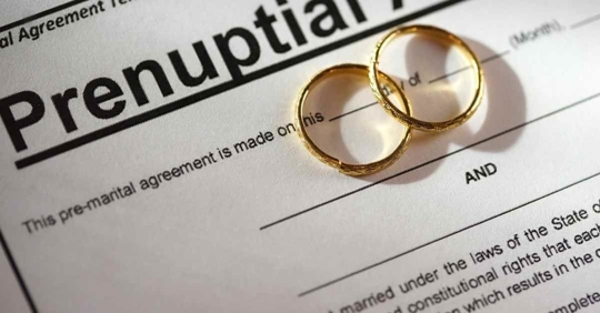 A pair of gold wedding bands resting on a prenuptial agreement