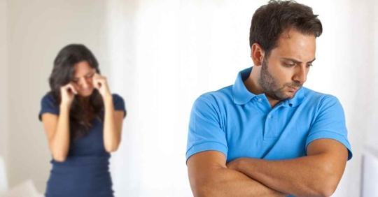 A man standing with his back to his wife and his arms crossed. The woman appears to be crying