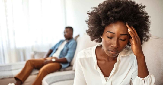 A woman appearing distressed as her husband sits in the background