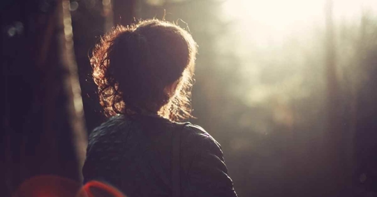 A woman sitting in a peaceful area. The sun is shining, and she looks very relaxed