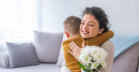 A mother hugging her son. She is also holding flowers