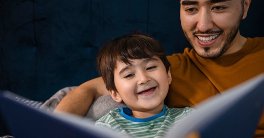 A child lying in bed while his father reads him a bedtime story.