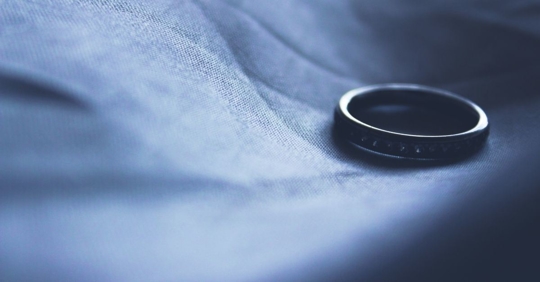 A wedding ring sitting on a sheet, as if someone had just taken it off
