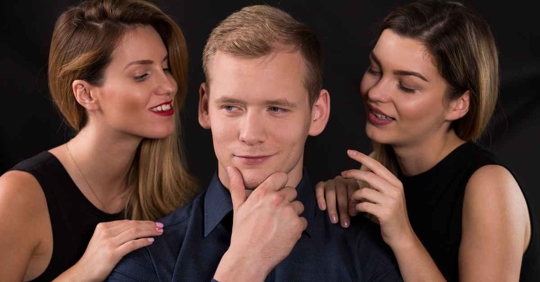 A man standing with a grin on his face. There is a woman on each side of him