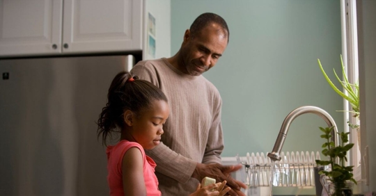 A father and his daughter washing dishes at the kitchen sink